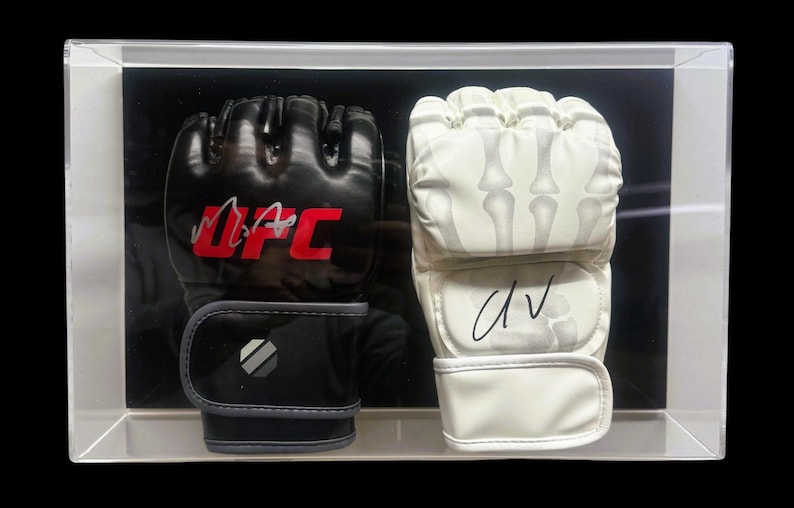 May include: A pair of signed boxing gloves in a clear display case. The black glove has "UFC" written in red and a signature. The white glove has a skeleton design and a signature.
