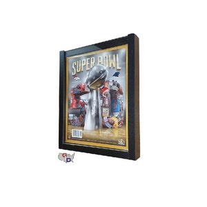 May include: A black framed picture of a Super Bowl magazine cover. The cover features a silver Super Bowl trophy with a football on top. The trophy is surrounded by players and fans. The text "SUPER BOWL" is printed in gold letters on the cover.