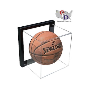 May include: A brown basketball with white stitching and the Spalding logo is displayed in a clear acrylic cube with a black frame. The cube is on a white background.