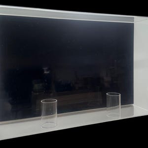 May include: A clear acrylic display case with two clear acrylic cylinders inside. The case has a black background.