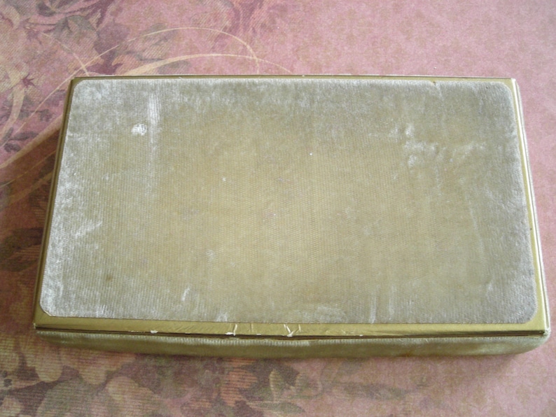 K&ouml;nnte beinhalten: Rechteckige Vintage-Box mit goldfarbenem Metallrahmen und hellgr&uuml;nem Samtdeckel. Die Box hat ein schlichtes, elegantes Design, und der Samt weist Gebrauchsspuren auf.