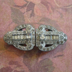 May include: A pair of silver-toned metal shoe clips with a decorative design of clear rhinestones.