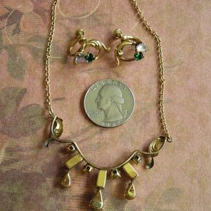 K&ouml;nnte beinhalten: Ein Vintage-Schmuckset in Goldt&ouml;nen mit einer Halskette und passenden Ohrringen. Die Halskette hat ein geschwungenes Design mit rechteckigen und tropfenf&ouml;rmigen Akzenten. Die Ohrringe haben ein florales Design mit gr&uuml;nen und rosa Edelsteinen.