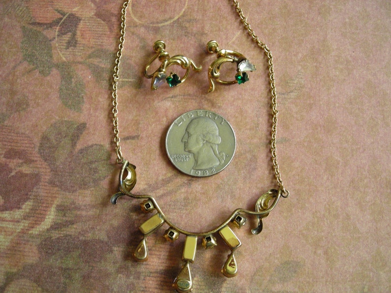 K&ouml;nnte beinhalten: Ein Vintage-Schmuckset in Goldt&ouml;nen mit einer Halskette und passenden Ohrringen. Die Halskette hat ein geschwungenes Design mit rechteckigen und tropfenf&ouml;rmigen Akzenten. Die Ohrringe haben ein florales Design mit gr&uuml;nen und rosa Edelsteinen.