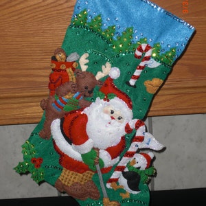 May include: A green and blue Christmas stocking with a Santa Claus figure holding a golf club. The stocking is decorated with a reindeer, a penguin, and a candy cane. The stocking is made of felt and has a sparkly finish.