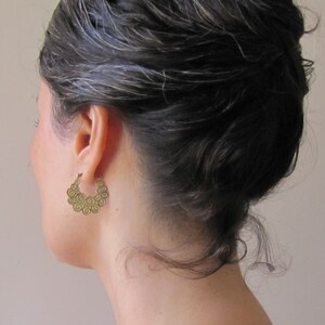May include: A pair of gold hoop earrings with a swirling, textured design. The earrings are worn by a person with dark hair.