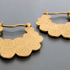 May include: A pair of gold hoop earrings with a swirling pattern. The earrings are made of metal and have a smooth finish.