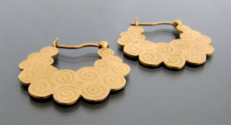 May include: A pair of gold hoop earrings with a swirling pattern. The earrings are made of metal and have a smooth finish.