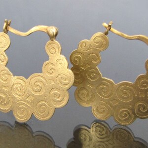 May include: A pair of gold hoop earrings with a swirling, textured design. The earrings are made of a smooth, shiny metal and have a simple, elegant style.