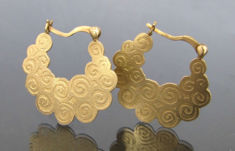 May include: A pair of gold hoop earrings with a swirling, textured design. The earrings are made of a smooth, shiny metal and have a simple, elegant style.