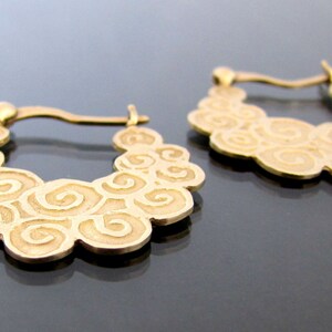 May include: A pair of gold hoop earrings with a swirling, cloud-like design.