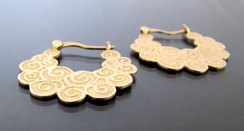May include: A pair of gold hoop earrings with a swirling, cloud-like design.