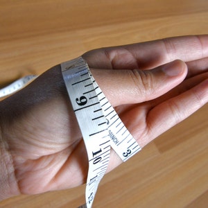 May include: A white measuring tape wrapped around a person's wrist, showing a measurement of 9 inches.