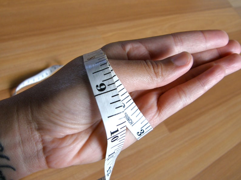 May include: A white measuring tape wrapped around a person's wrist, showing a measurement of 9 inches.