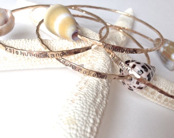 May include: Three gold hammered bangle bracelets with different Hawaiian words engraved on them. The bracelets are stacked on top of each other and are resting on a white starfish.