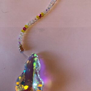 May include: A clear crystal teardrop prism with iridescent rainbow colors hanging from a beaded chain with clear, yellow, and pink beads.