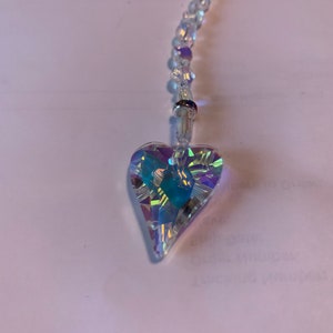 May include: A crystal heart charm hangs from a clear crystal beaded chain. The heart is iridescent and has a faceted design.