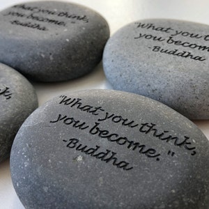 May include: Three gray stones with the quote "What you think, you become." inscribed on them. The quote is attributed to Buddha.