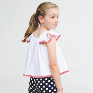 May include: A white sleeveless top with red and white striped trim around the neckline and sleeves. The top is paired with black and white polka dot shorts with red and white striped trim around the waistband and legs.