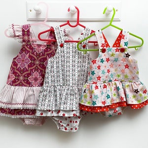 May include: Three girls' dresses with different patterns and colors. The first dress is pink and white with a floral pattern. The second dress is gray and white with a striped pattern. The third dress is white with a red, green, and blue star pattern.
