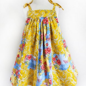 May include: A yellow, blue, and white floral print sundress with thin straps that tie at the shoulders. The dress has a gathered bodice and a full skirt.