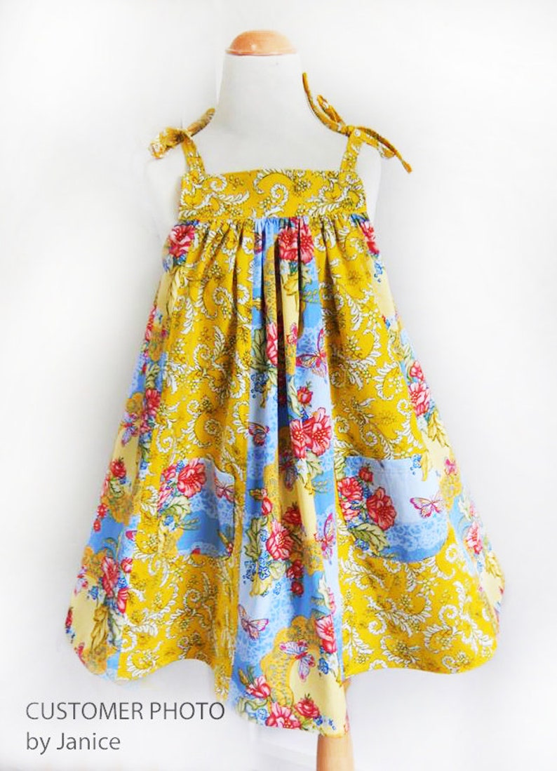 May include: A yellow, blue, and white floral print sundress with thin straps that tie at the shoulders. The dress has a gathered bodice and a full skirt.