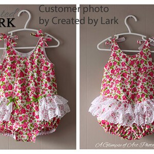 May include: A white floral print baby onesie with a white lace ruffle trim. The onesie is hanging on a white hanger.