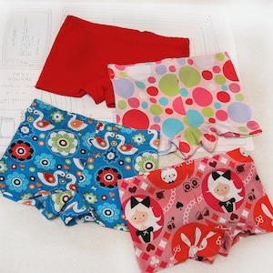 Può includere: Quattro paia di biancheria intima di cotone colorata con diversi motivi. I motivi includono pois, cigni, fiori e una ragazza dei cartoni animati con un coniglio.