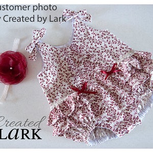 May include: A white and red floral print baby girl's romper with a ruffled skirt and a matching headband. The romper has a sleeveless design and a gathered waist.