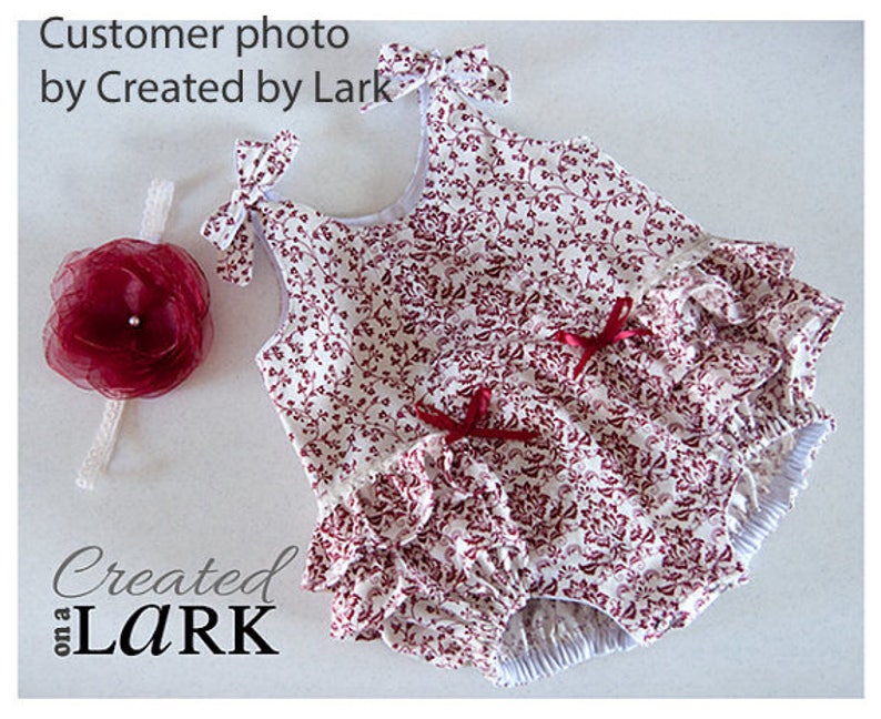 May include: A white and red floral print baby girl's romper with a ruffled skirt and a matching headband. The romper has a sleeveless design and a gathered waist.