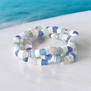 May include: A layered bracelet made with white and blue sea glass beads. The bracelet is made with a variety of shades of blue and white beads, and is accented with silver beads.