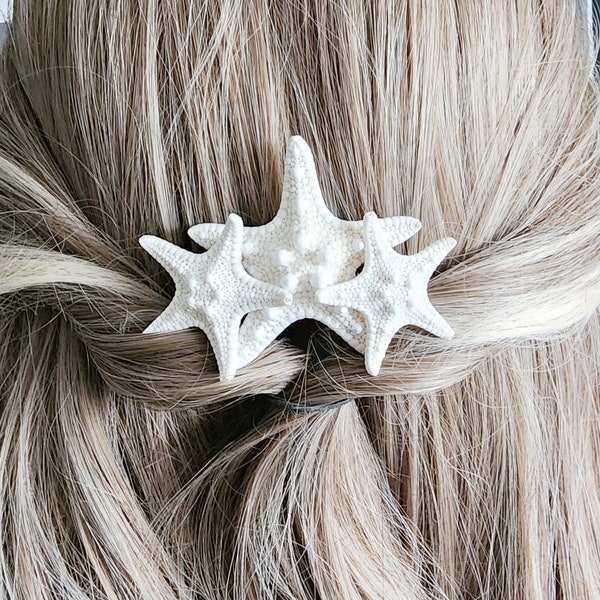 May include: Three white starfish hair clips arranged in a cluster. The clips are made of white ceramic and have a textured surface. The clips are attached to a brown hair tie.
