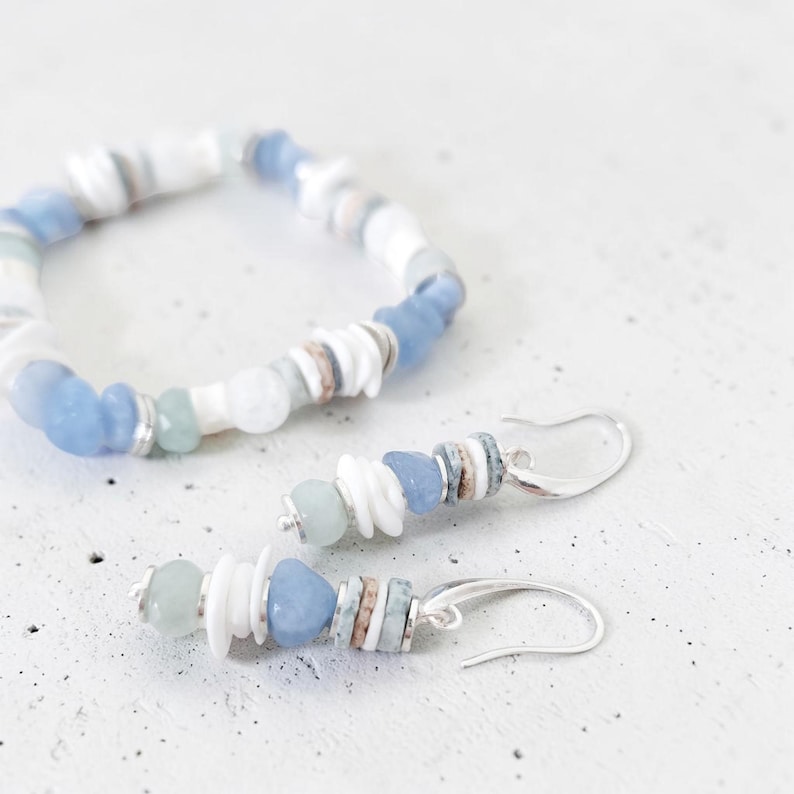 May include: A bracelet and matching earrings set. The jewelry features a combination of white, light blue, and silver beads. The earrings have a hook closure. The bracelet and earrings are made with a variety of shapes and sizes of beads.