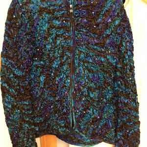 May include: A blue and black sequined jacket with a zipper closure. The jacket has a crinkled texture and is adorned with sequins.