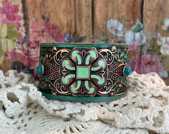 May include: A copper and green metal cuff bracelet with a decorative floral design and two turquoise stones.