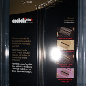 Peut inclure: Deux aiguilles à tricoter argentées avec un emballage en plastique noir. L'emballage porte le texte "addiclick" et "Luxus für die Hände Indulge your hands" en allemand et en anglais. L'emballage montre également différents types d'aiguilles à tricoter, notamment les aiguilles de base, en bambou, en dentelle à bouts courts et en dentelle à bouts longs.