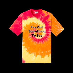 May include: A tie-dye t-shirt in a spiral pattern of red, orange, and yellow. The shirt features the text "I've Got Something To Say" in black block letters. The shirt has short sleeves and a crew neck.