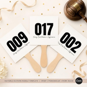 Può includere: Tre palette da asta quadrate bianche con manici in legno chiaro, ciascuna con grandi numeri neri 009, 017 e 002, e il testo Every Bid Makes a Difference. Un martello da asta in legno scuro è posizionato nell'angolo in alto a destra.