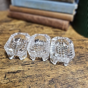 May include: Three small, clear glass dishes with a rectangular shape and rounded corners. Each dish features a textured, grid-like pattern on the interior base and stands on four short, sturdy feet, crafted from transparent pressed glass.