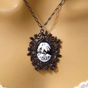 May include: A black cameo necklace with a white cameo featuring a palm tree and a bird. The cameo is set in a black filigree frame.