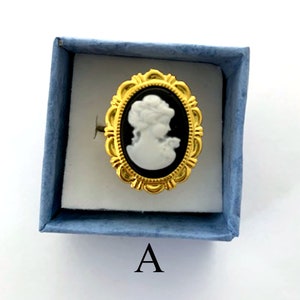 May include: A gold ring with a black and white cameo of a woman's profile. The ring is in a blue velvet box with the letter "A" printed on the bottom.