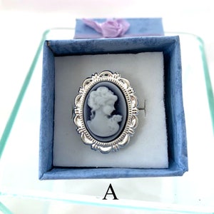 May include: A silver ring with a blue cameo featuring a woman's profile. The ring is in a blue velvet box with the letter "A" printed on the bottom.