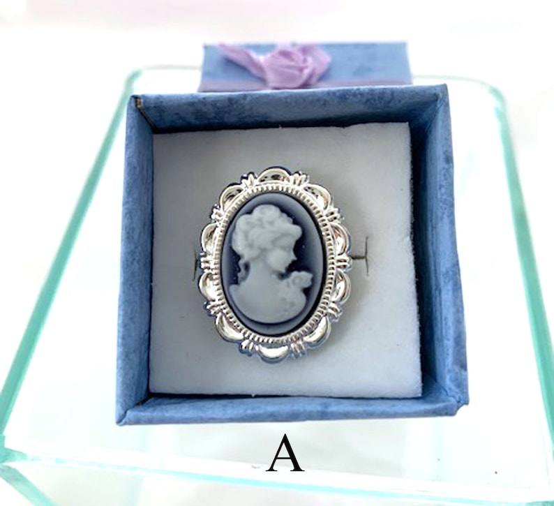 May include: A silver ring with a blue cameo featuring a woman's profile. The ring is in a blue velvet box with the letter "A" printed on the bottom.