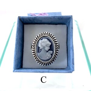 May include: A silver ring with a blue cameo featuring a woman's profile. The ring is in a blue velvet box with the letter "C" printed on the bottom.