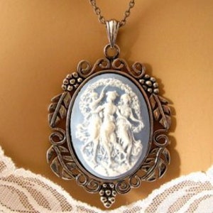 Op de afbeelding: Een zilverkleurige ketting met een hanger met een blauwe en witte cameo met drie vrouwen die in een cirkel dansen.