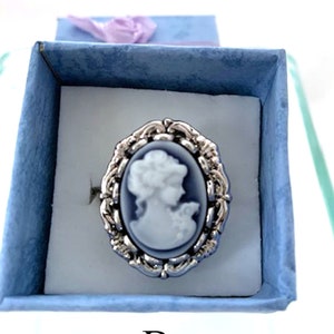 May include: A silver ring with a blue and white cameo featuring a woman's profile. The ring is in a blue velvet box with the letter "B" printed on the bottom.