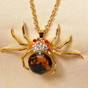 May include: A gold-tone spider pendant necklace with a brown crystal body and clear rhinestone accents. The spider has red eyes.