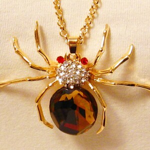 May include: A gold-tone spider pendant necklace with a large, faceted, brown gemstone body and clear rhinestone accents. The spider has red rhinestone eyes.