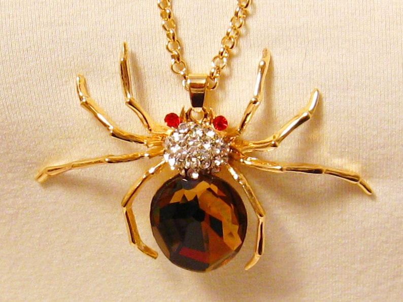 May include: A gold-tone spider pendant necklace with a large, faceted, brown gemstone body and clear rhinestone accents. The spider has red rhinestone eyes.