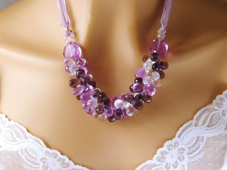 K&ouml;nnte beinhalten: Eine violette, klare und braune Kristallperlenkette mit einer Lavendelband-Schleife.